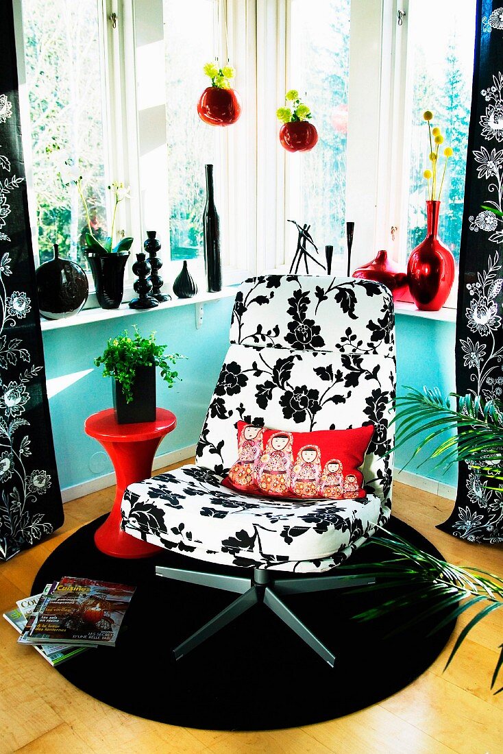 Drehsessel mit schwarz-weißem Blumenmuster auf rundem Teppich in Zimmerecke, auf Fensterbank Vasensammlung in Schwarz und Rot