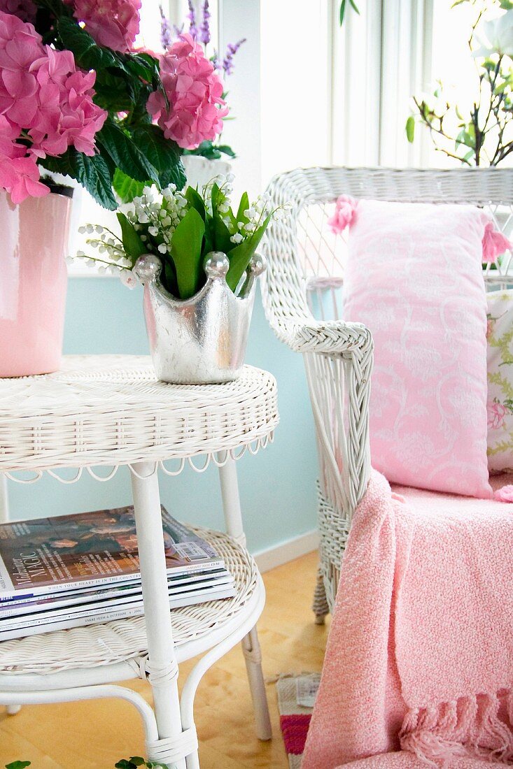 Weisser Rattan Beistelltisch mit Blumenvasen, daneben passender Sessel mit rosa gemustertem Kissen