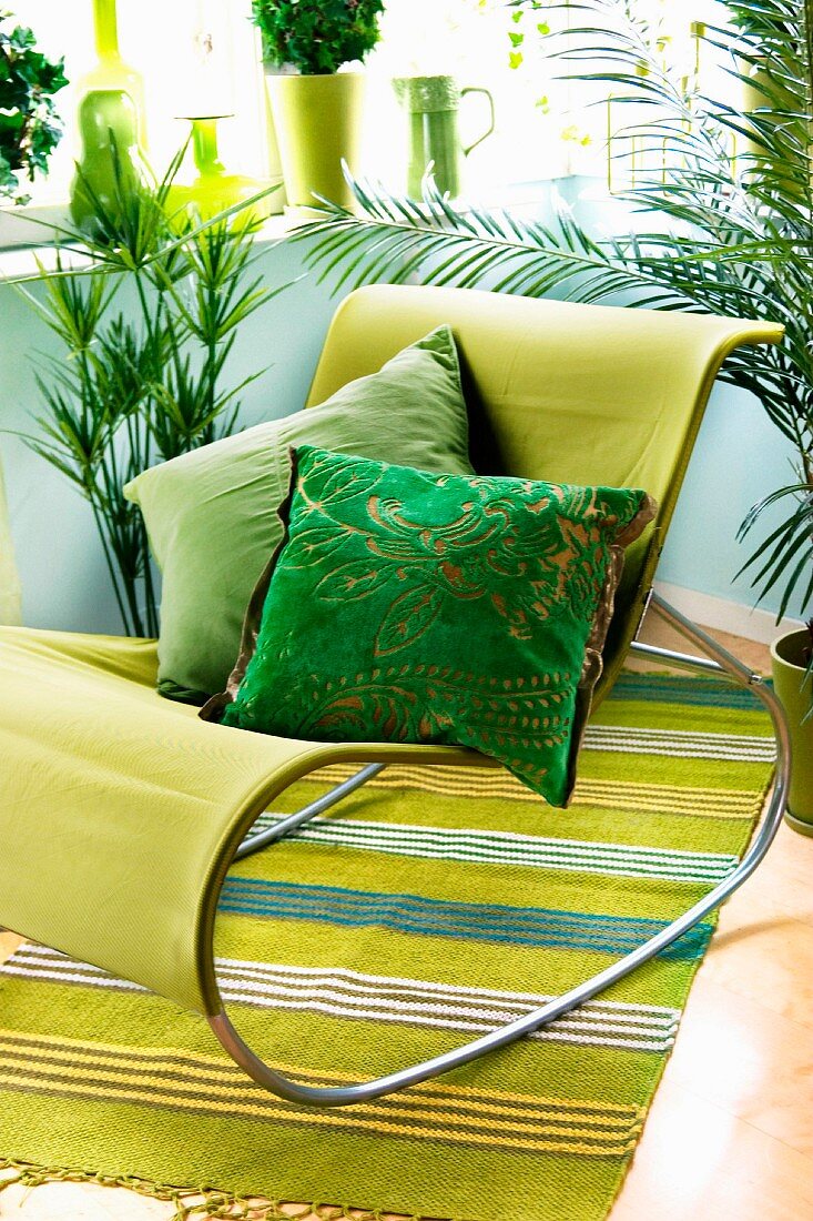 Modern rocking chair with green cover and scatter cushions in shades of green on striped rug