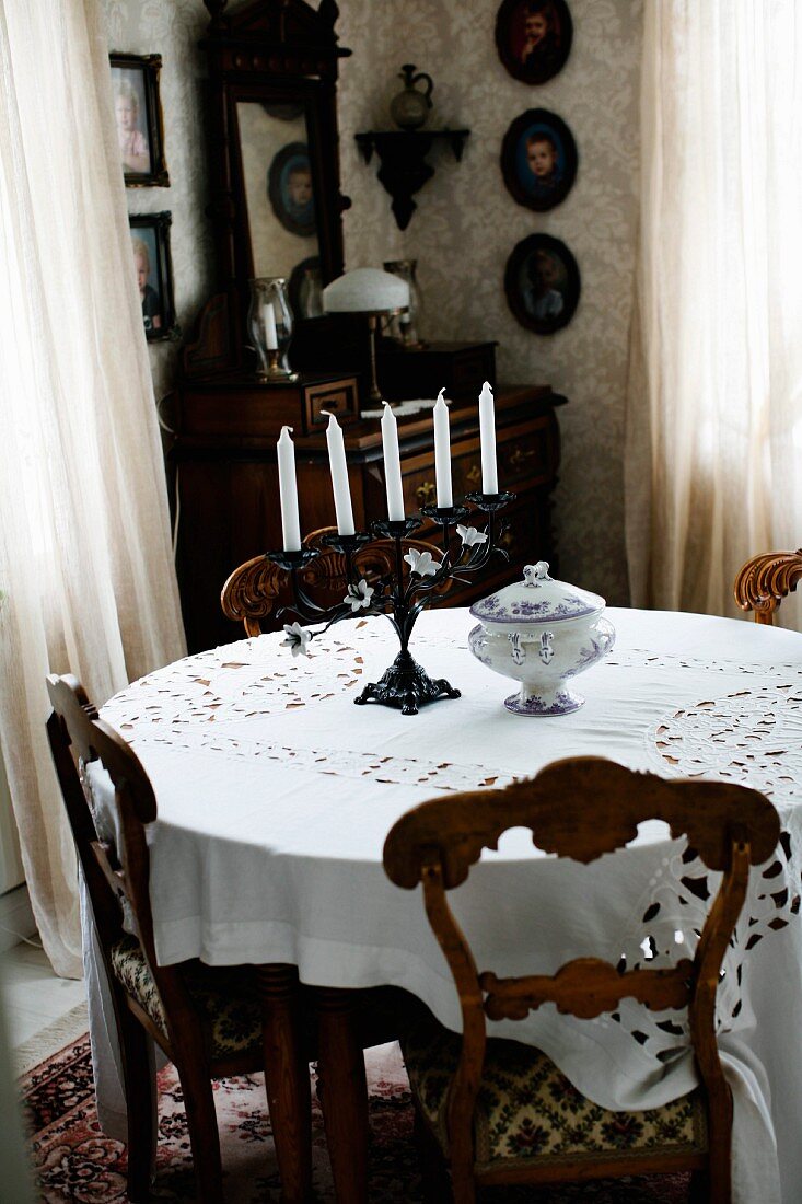 Stühle mit geschnitzter Rückenlehne um rundem Tisch mit weisser Tischdecke, in traditioneller Zimmerecke