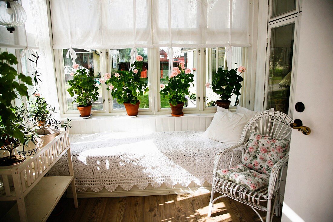 Weisser Rattan Sessel und Tagesliege mit Spitzendecke vor Fenster, Blumentöpfe auf Fensterbank in Loggia