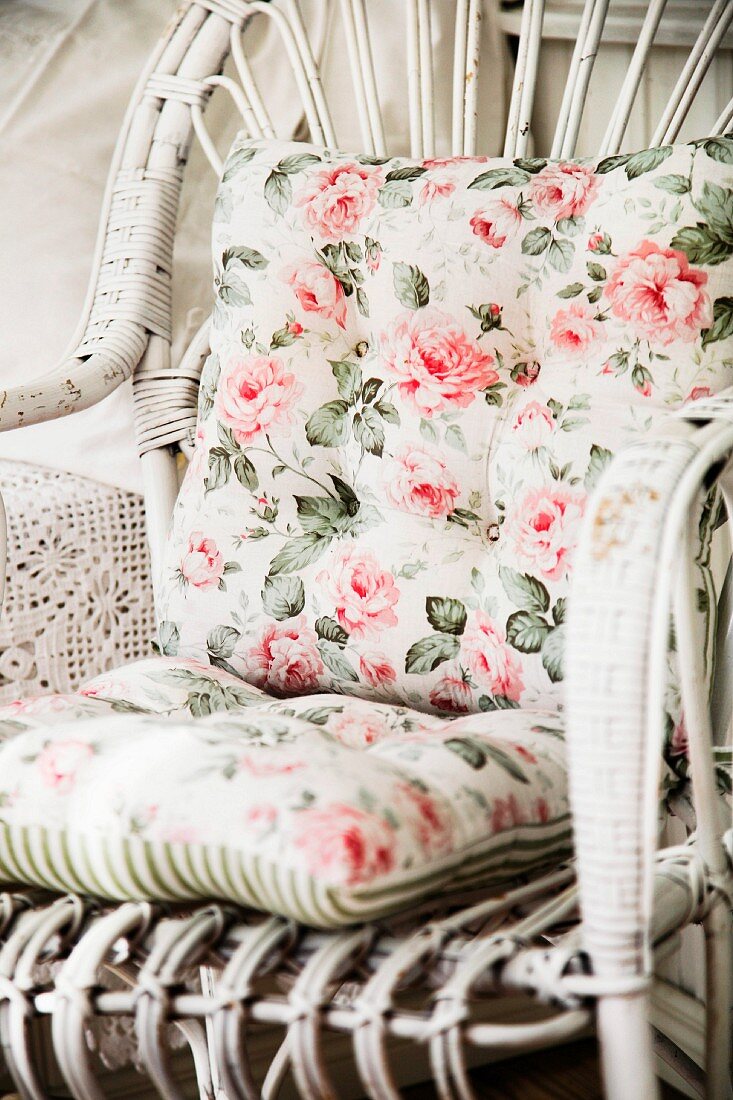 Nostalgic, floral cushions on white-painted rattan chair