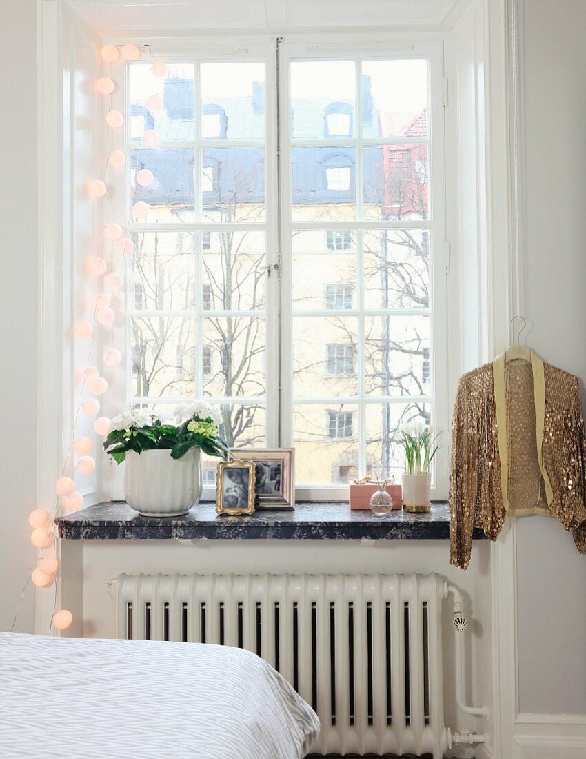 Sprossenfenster mit weisser Lampiongirlande und goldfarbene aufgehängte Paillettenjacke in städtischem Landhaus-Schlafzimmer