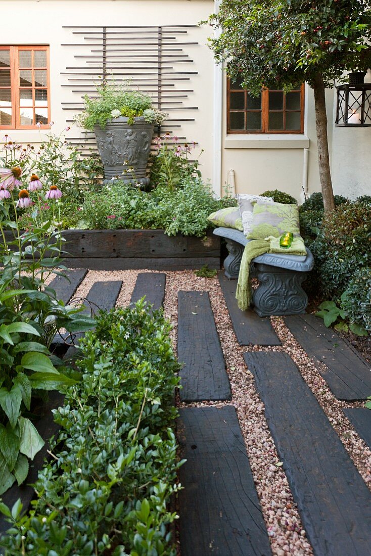 Flooring made from dark wooden sleepers and gravel in courtyard with planters and trellising on house facade