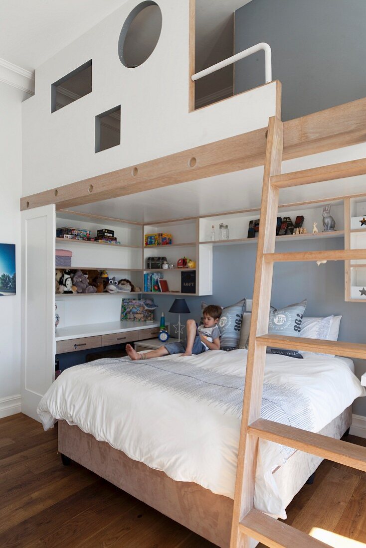 Kinderzimmer mit Galerie über Bett und kleinem Jungen, Wandregale, seitlich Leiter