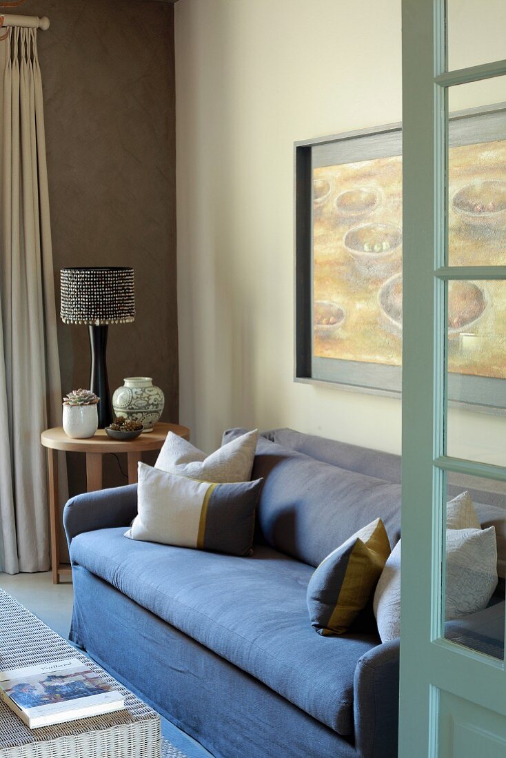 Offene Tür und Blick auf blaue Couch neben Beistelltisch mit Tischleuchte in Zimmerecke