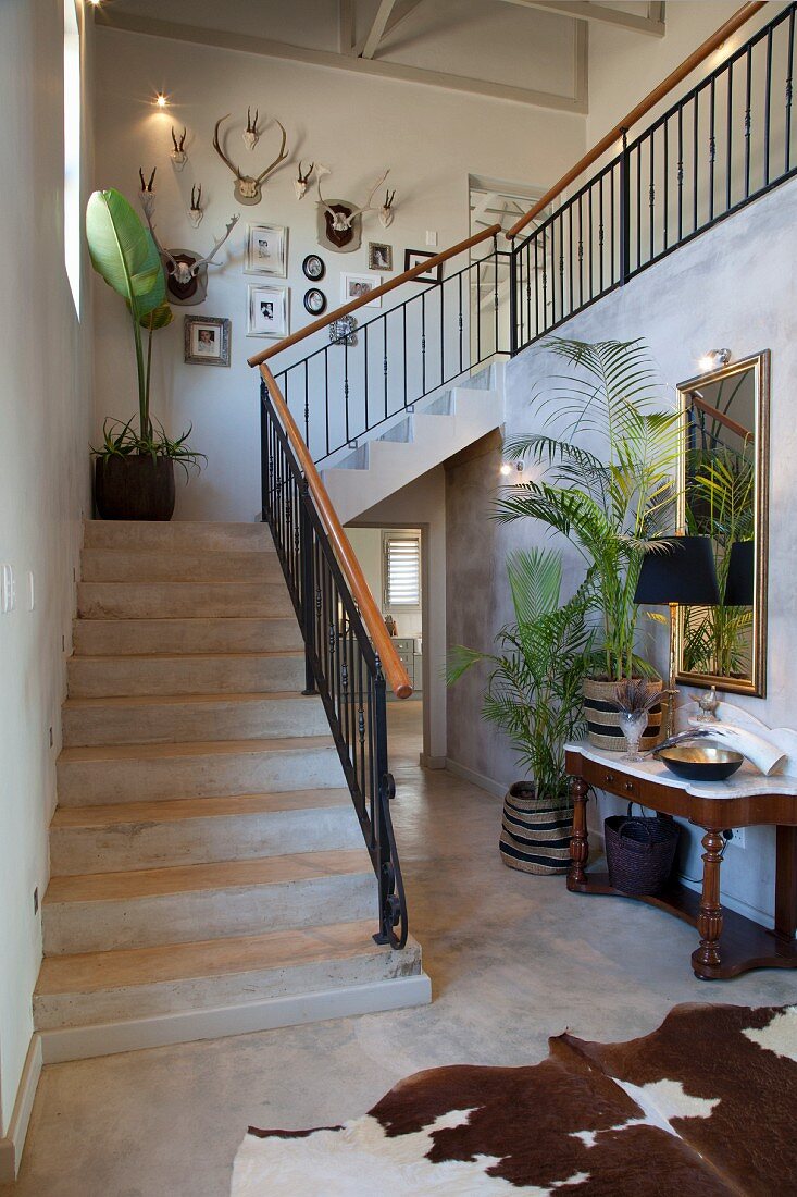 Treppenaufgang in offenem Hausflur mit Tierfellteppich, im Hintergrund antiker Wandtisch und Zimmerpalmen