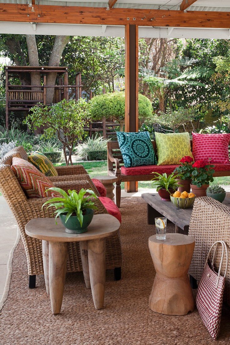 Möblierte Terrasse, seitlich Rattansessel, im Hintergrund Sitzbank mit verschiedenfarbigen Kissen