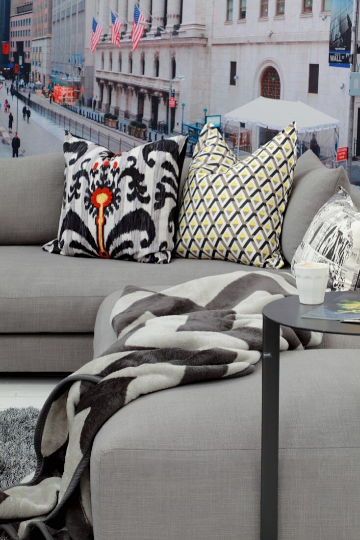 Patterned scatter cushions on pale grey sofa in front of New York mural wallpaper