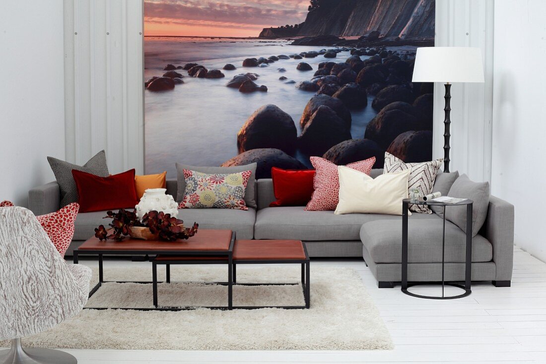 Set of coffee tables and grey sofa in front of mural wallpaper showing sunset on rocky coast