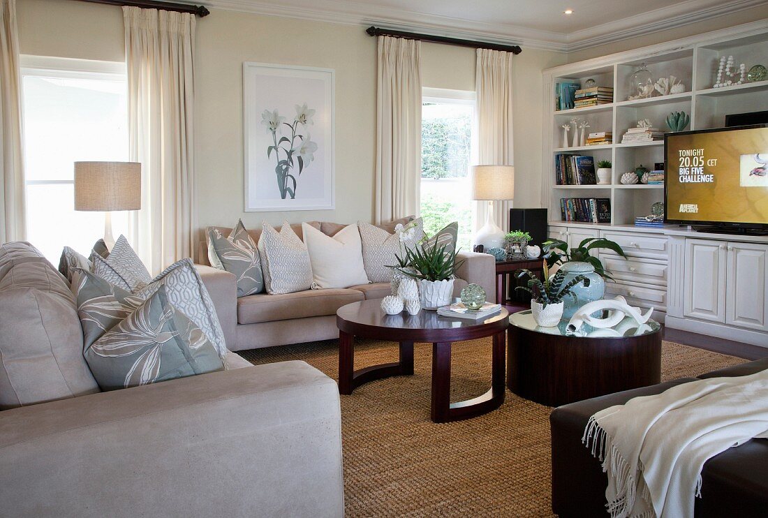 Elegantes Wohnzimmer mit cremefarbenen Sofas und zwei runden Couchtischen aus dunklem Holz