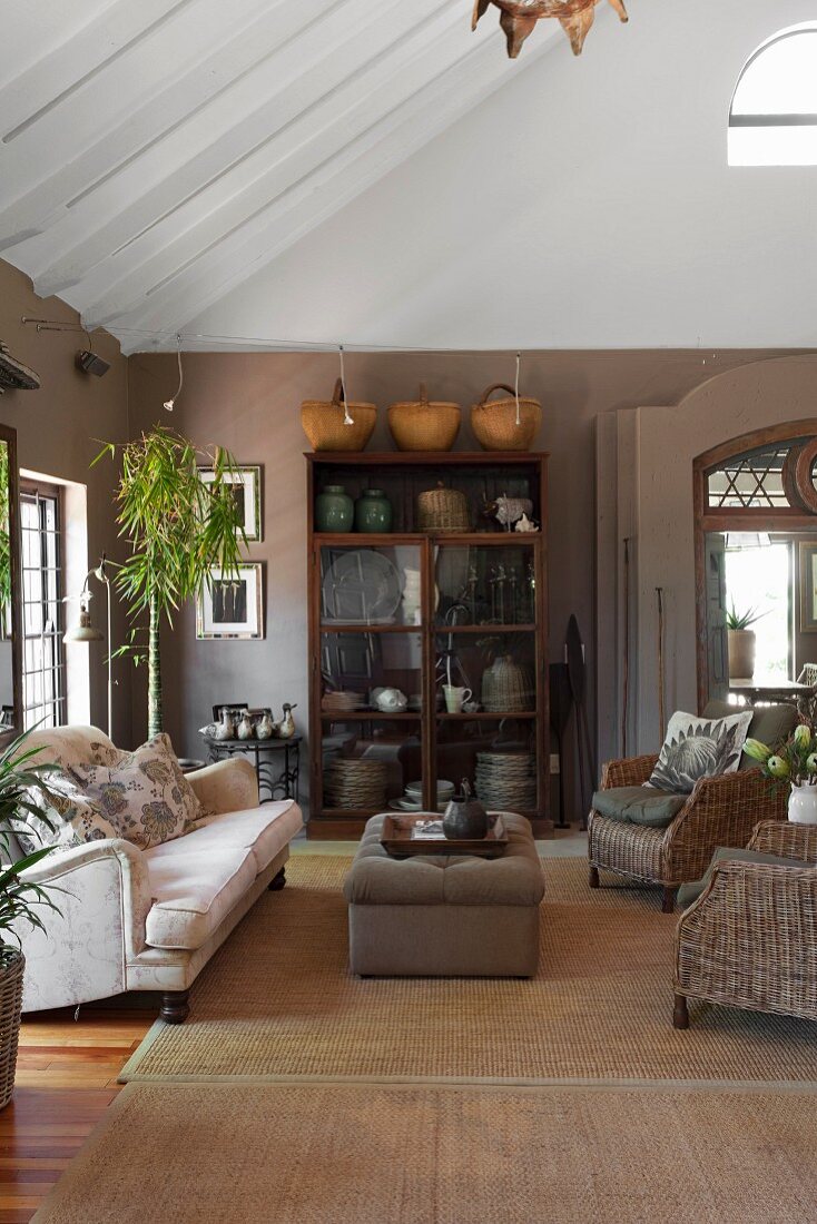 Korbstühle und Sofa auf Sisalteppich vor Vitrinenschrank im Wohnzimmer mit warmen Erdtönen