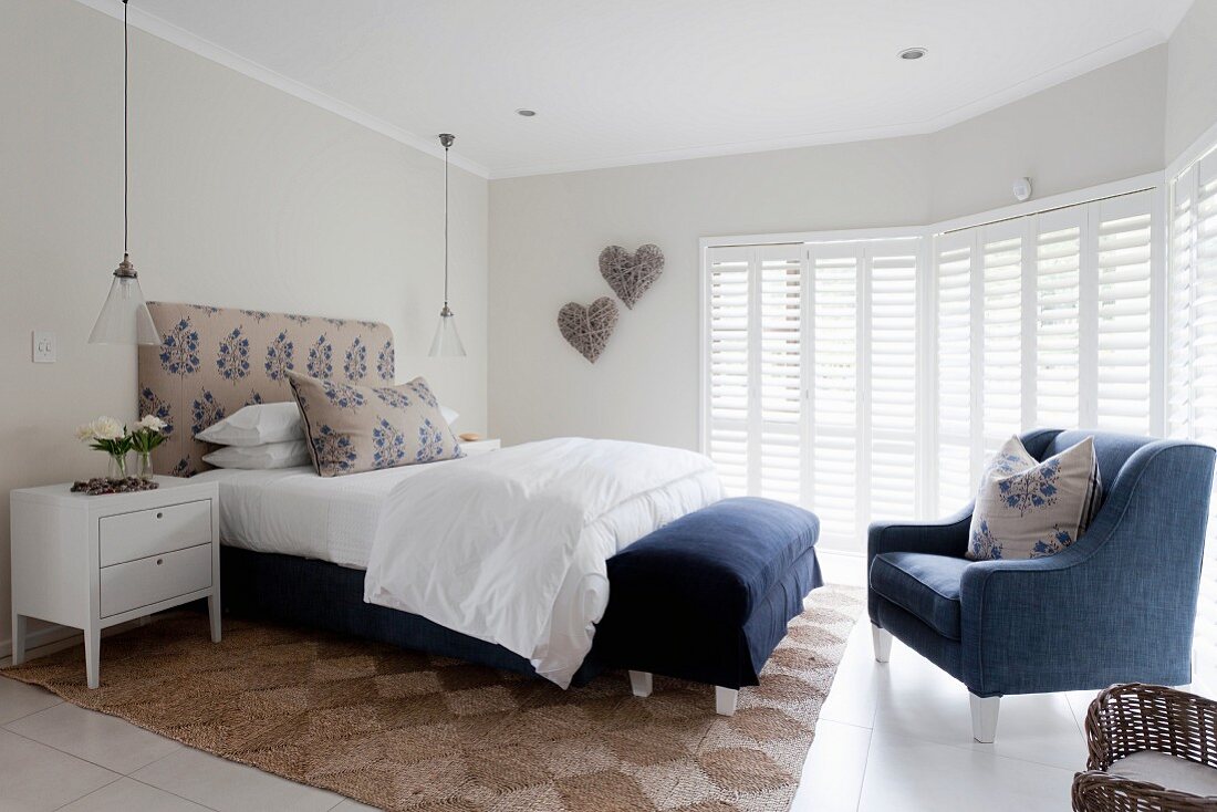 Elegantes Schlafzimmer mit weiss-blauen Farbakzenten, Sessel und Bank mit blauem Bezug an Bettende