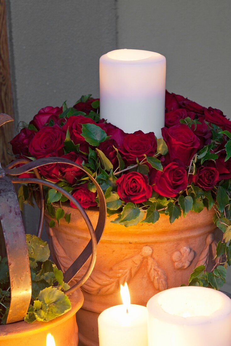 Mit Kerzenlicht angeleuchteter Blumentopf, mit weisser Kerze in Rosenbett