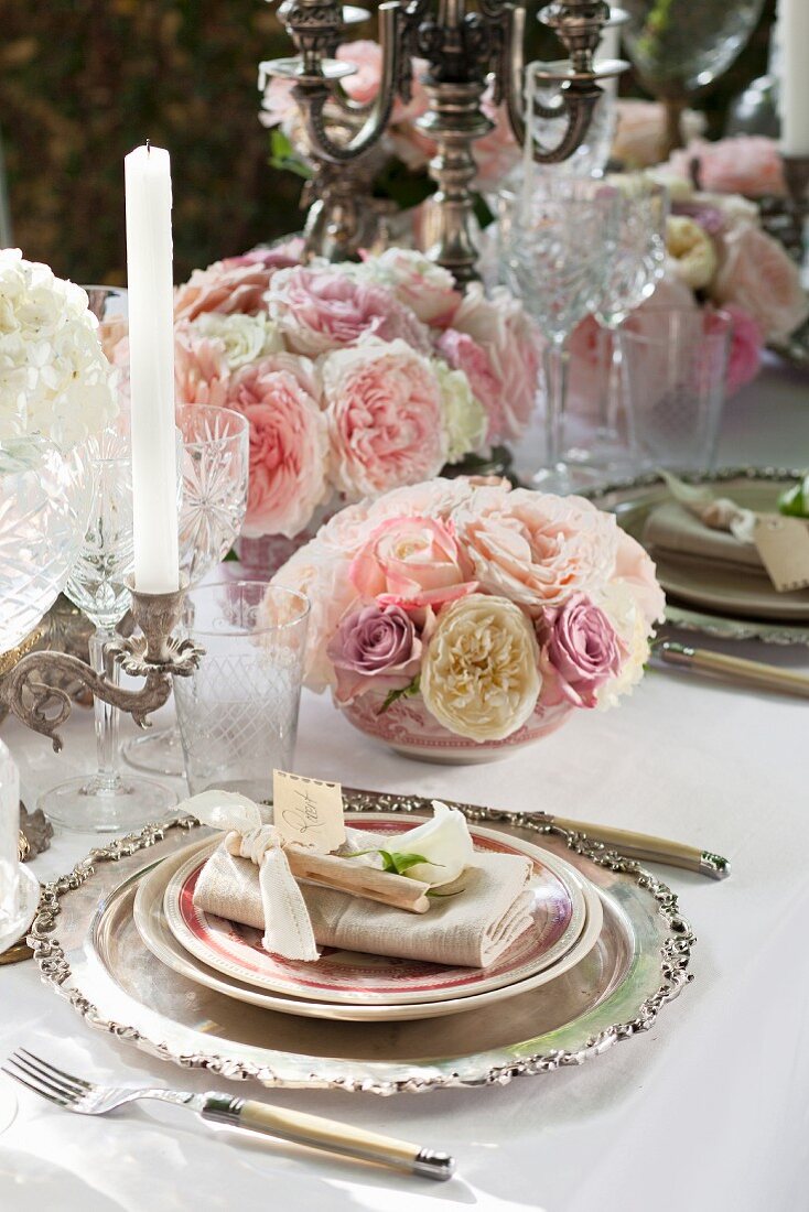 Elegantes Gedeck und Blumengestecke aus verschiedenfarbigen Rosenblüten auf festlichem Tisch