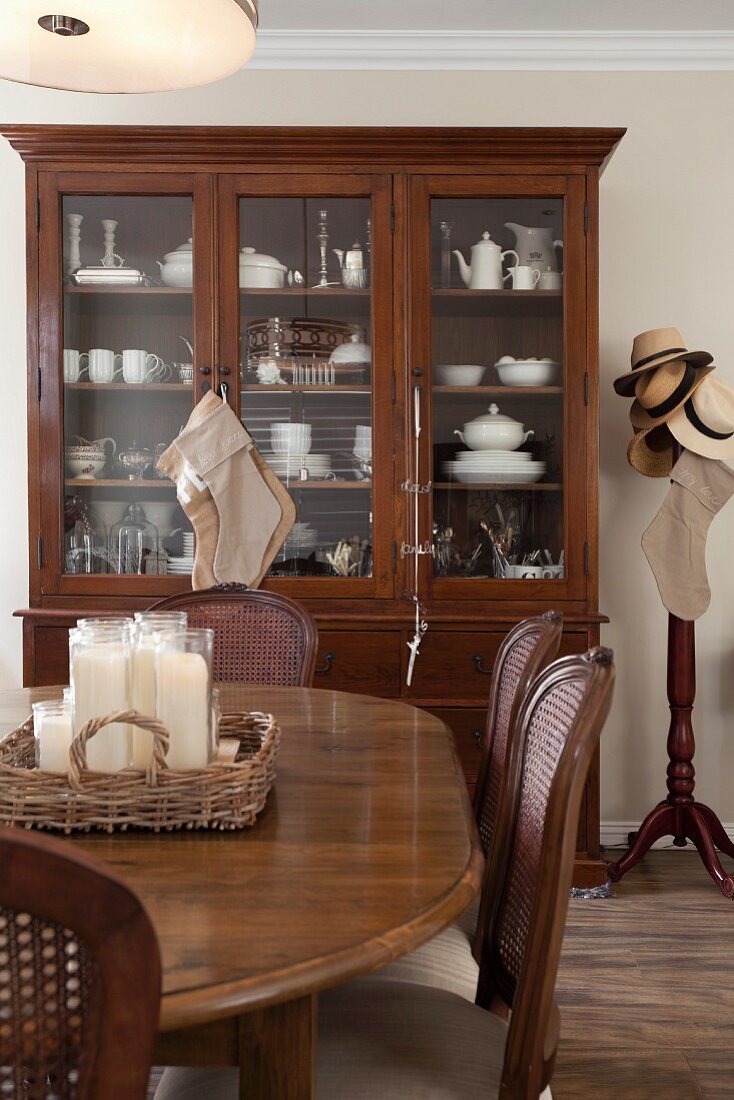 Dining area with antique chairs around wooden table in front of crockery in glass-fronted cabinet