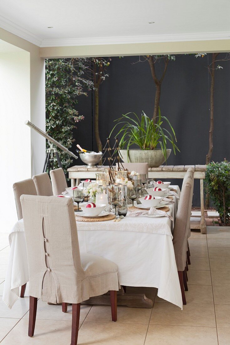 Stühle mit naturfarbener Husse um festlich gedeckten Tisch auf überdachter Terrasse