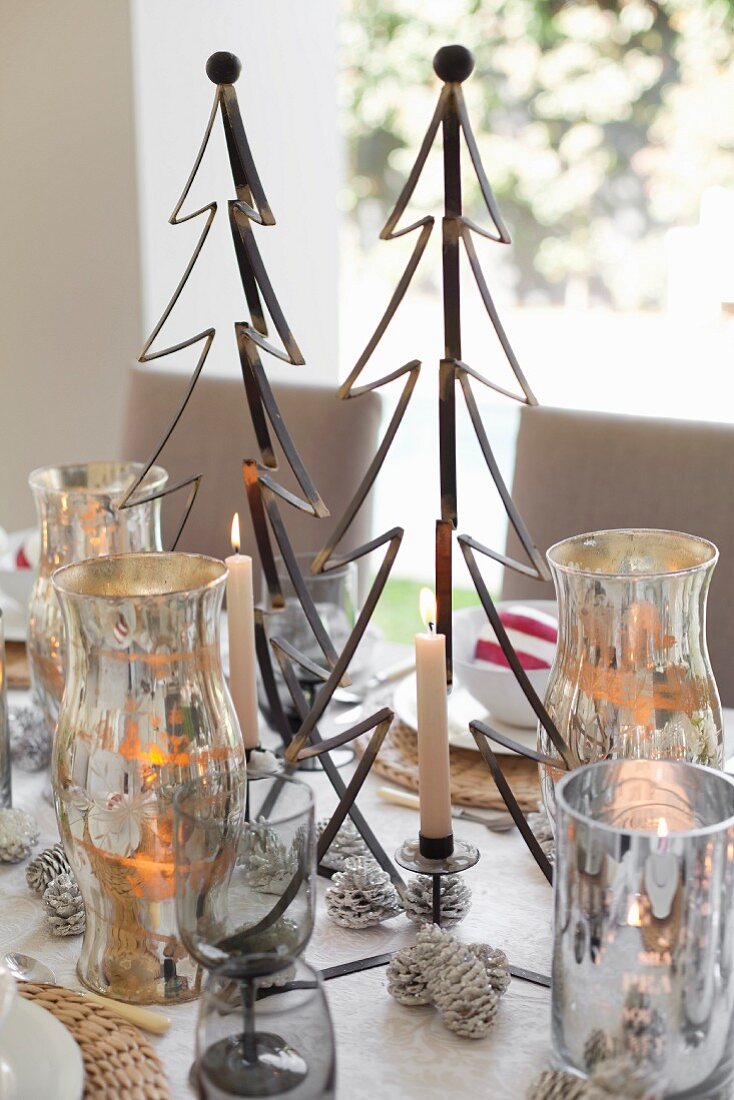 Brennende Kerze und Weihnachtsdekoration, stilisierter Tannenbaum aus Metall, zwischen Silber Windlichtern