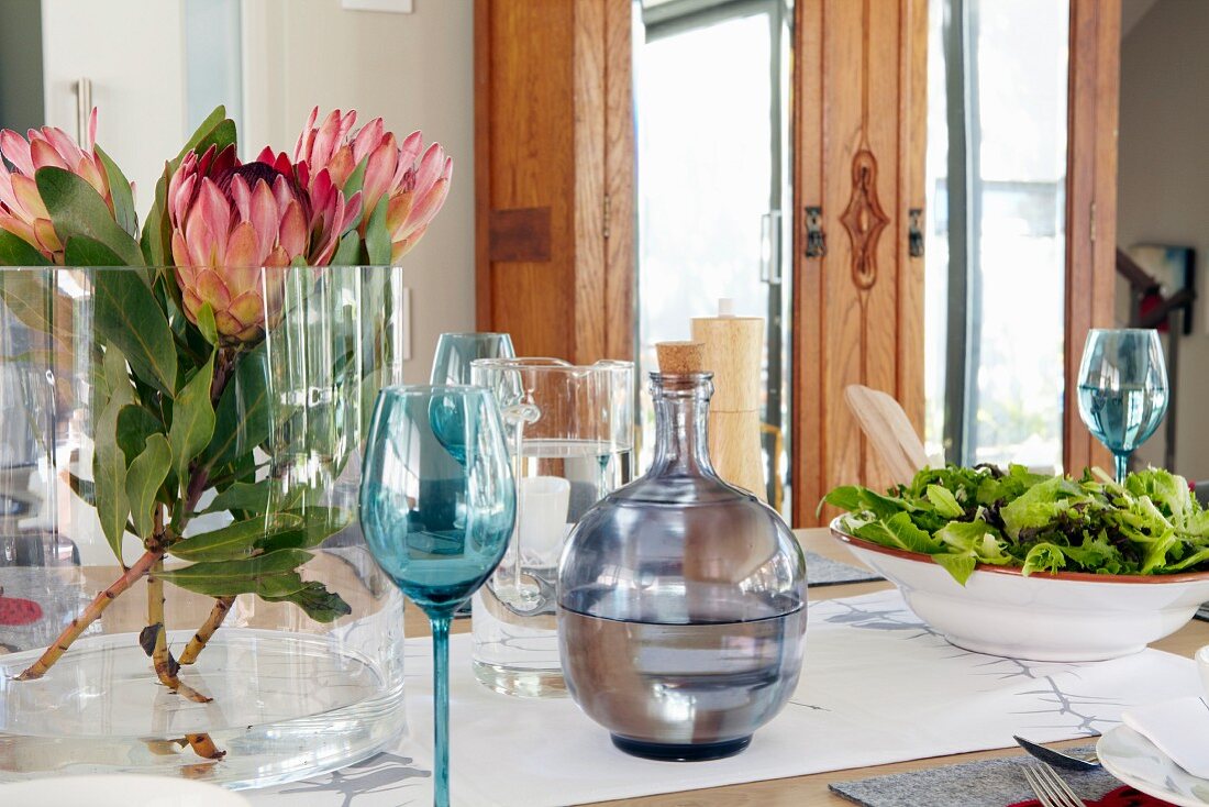 Protea in Glasvase und Salatschüssel auf gedecktem Tisch