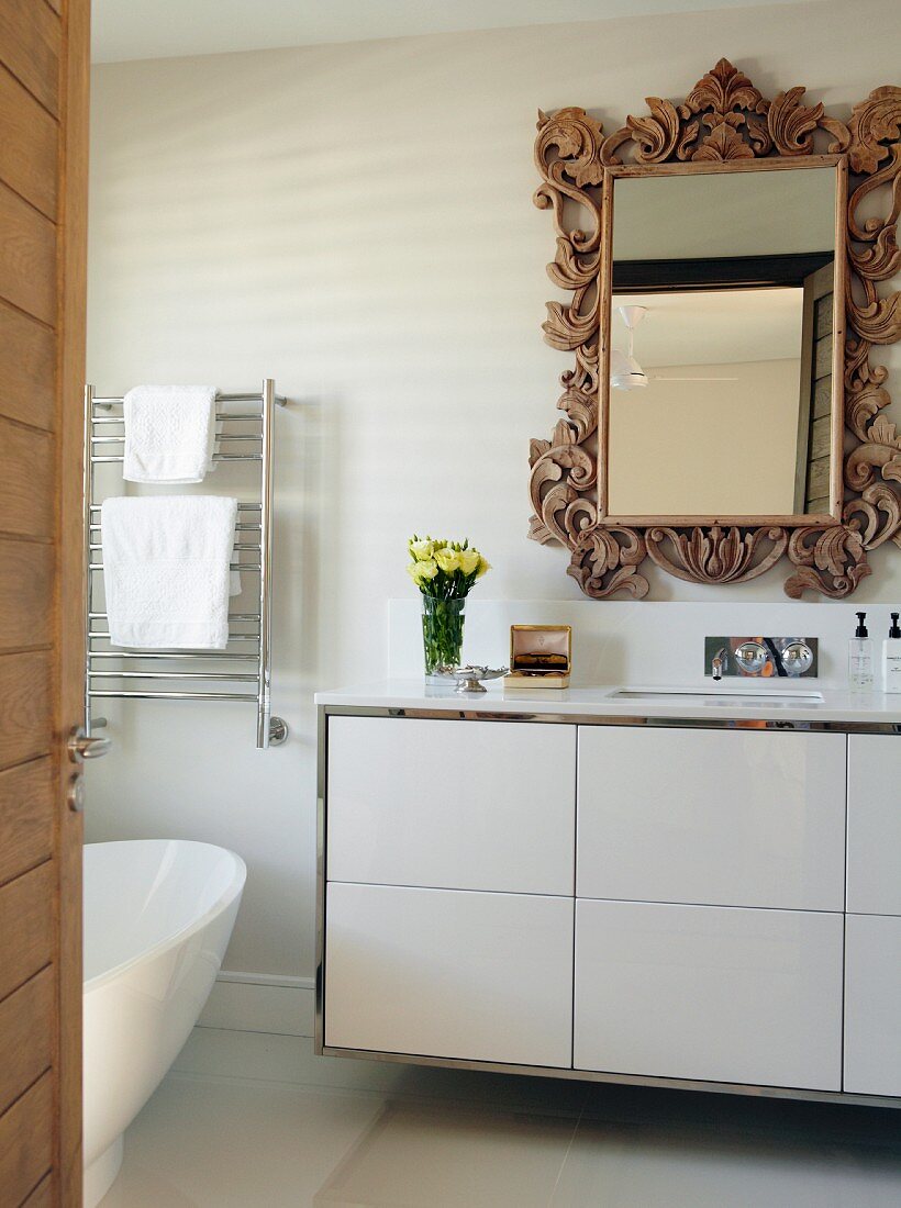 Blick durch offene Tür auf modernen Waschtisch mit weißem Unterschrank, Wandspiegel mit verziertem Holzrahmen