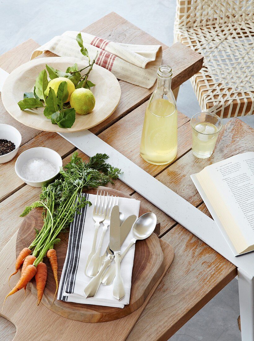 Holzbrett mit Besteck und Gemüse, Limonade und Zitronen auf Holztisch