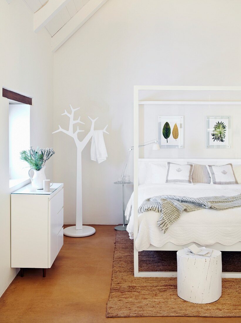 Double bed with white frame and clothes stand in shape of stylised tree in bright attic bedroom