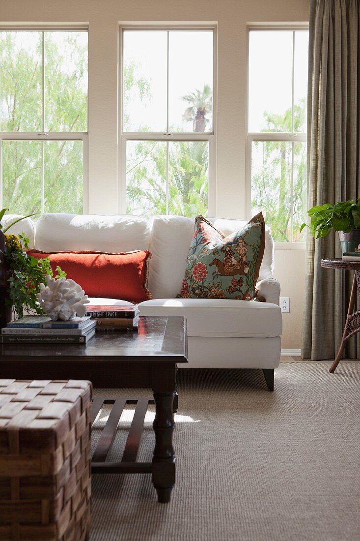 Wohnzimmer mit weisser Couch und Couchtisch vor Fenster mit Gartenblick
