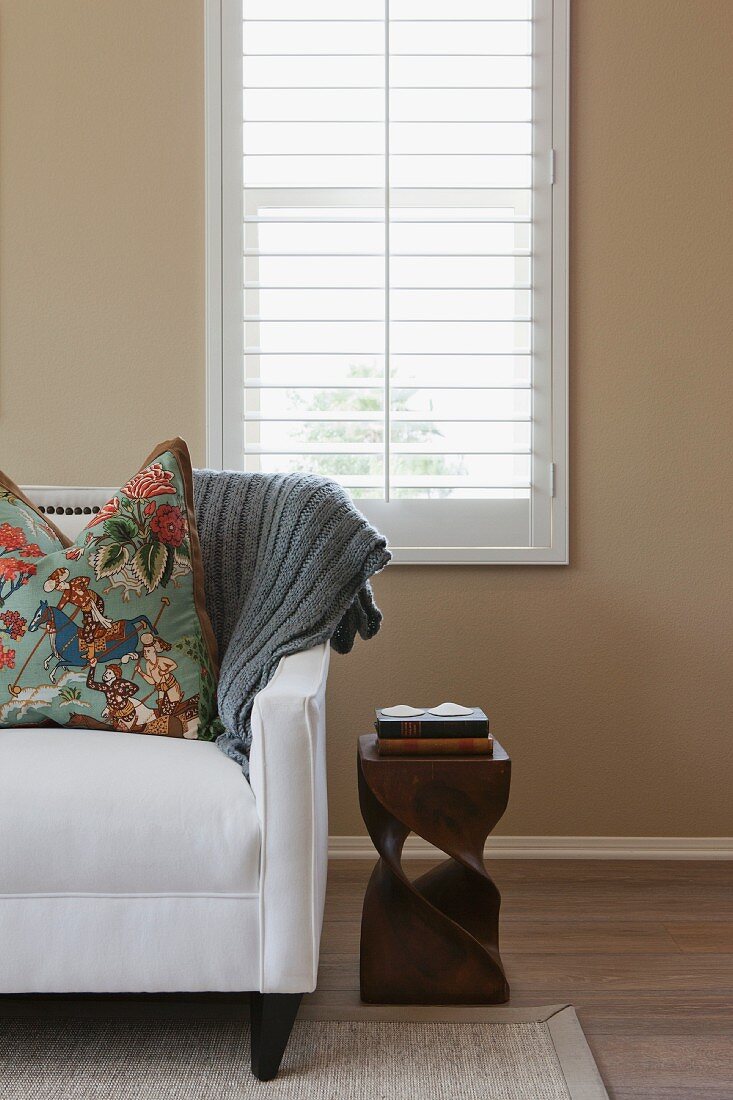 Teilweise sichtbare weiße Couch vor Fenster mit weisssen Innenladen und sandfarben getönter Wand