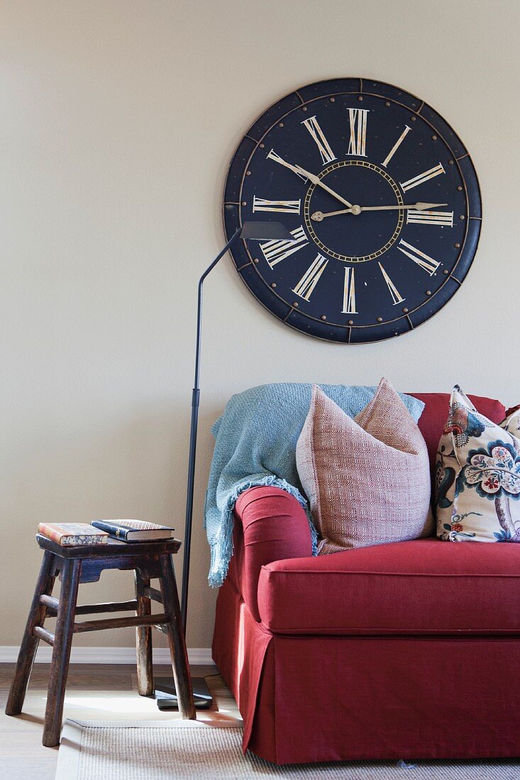 Bordeauxrote Couch und rustikaler Holzhocker vor Wand mit grosser Uhr und altem Zifferblatt