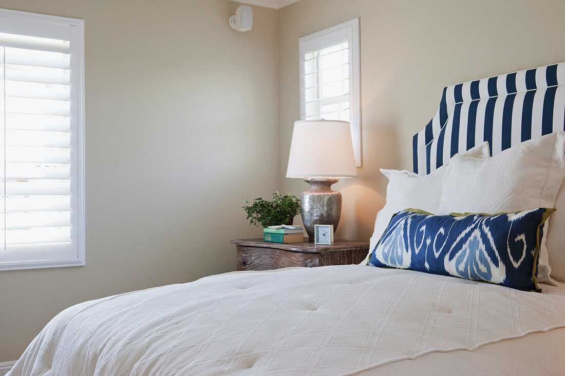 Kissenstapel auf Bett vor gepolstertem Kopfteil mit blauweissen Streifen in ländlichem Schlafzimmer