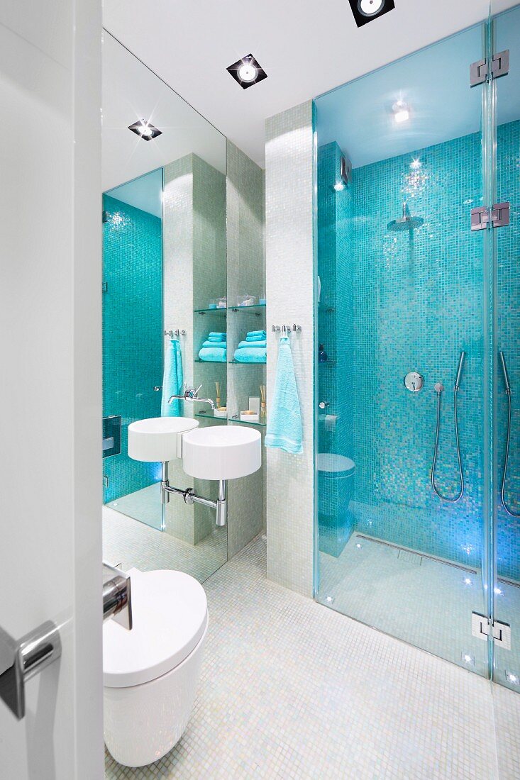 Sink mounted on mirrored wall next to glazed, floor-level shower area with pale blue mosaic tiles on wall