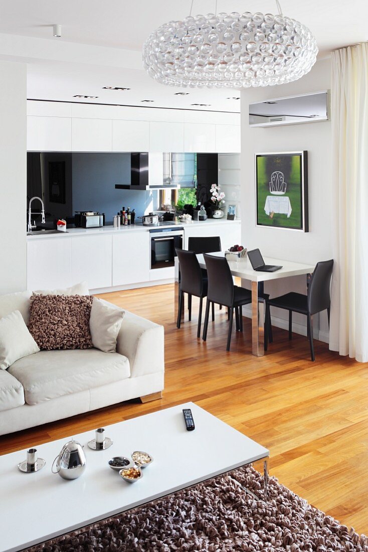 Weisser Couchtisch auf flokatiartigem Teppichläufer und helles Sofa, dahinter Essplatz an Wand in offener Einbauküche