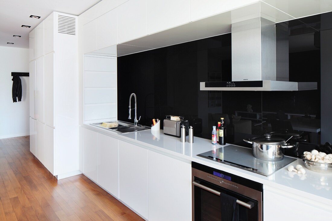 Coole, weiße Einbauküche mit schwarzer Glas Rückwand über Arbeitsplatte