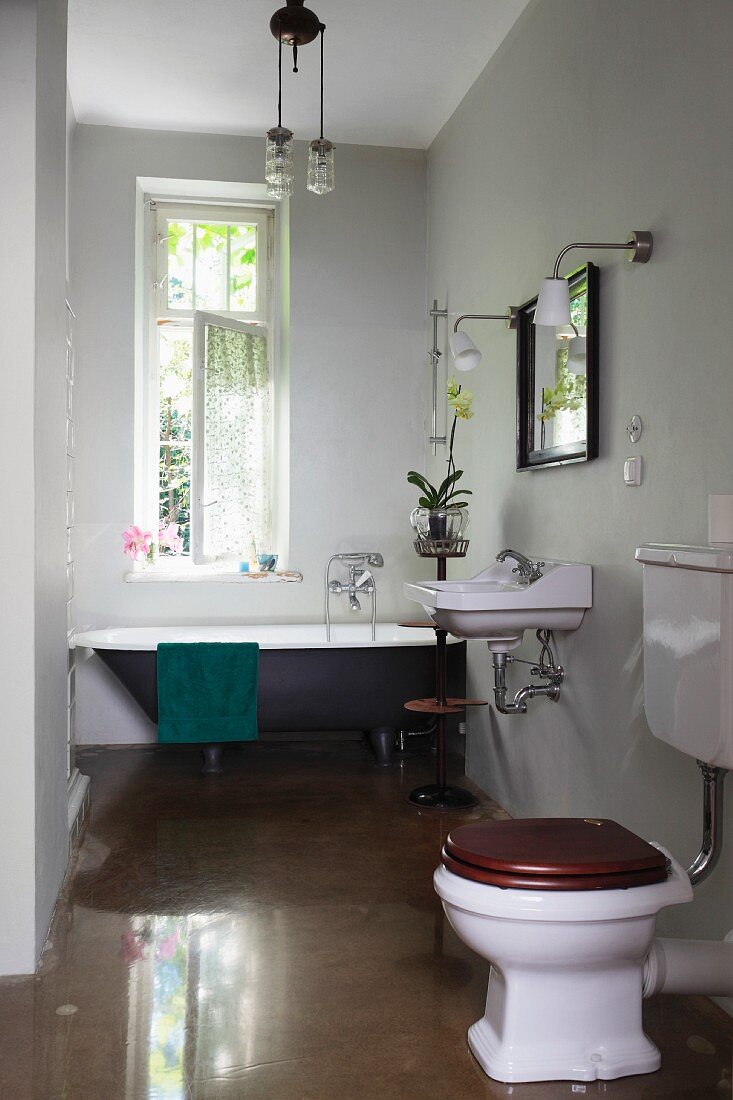 WC auf hochglänzendem Boden, im Hintergrund Vintage Badewanne am Fenster in graugetöntem Bad