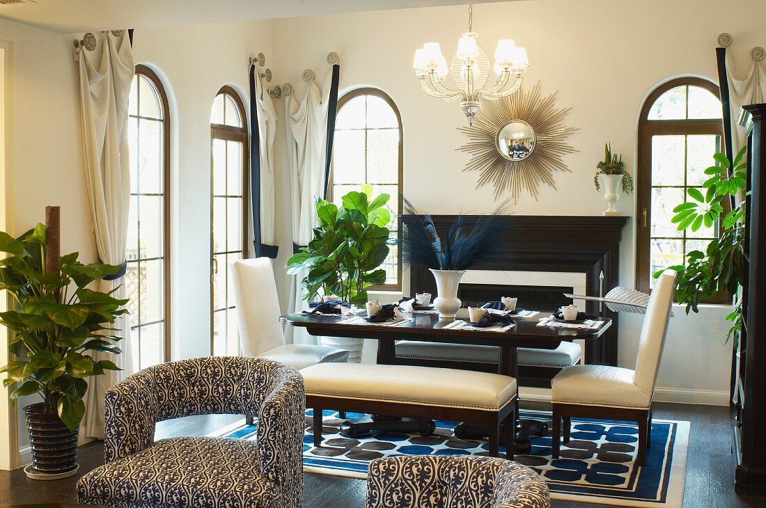 Gepolsterte Stühle mit weissblauem Ornamentmuster auf Bezug, im Hintergrund gedeckter Tisch und elegante, weissbezogene Stühle in Essbereich mit Rundbogentüren
