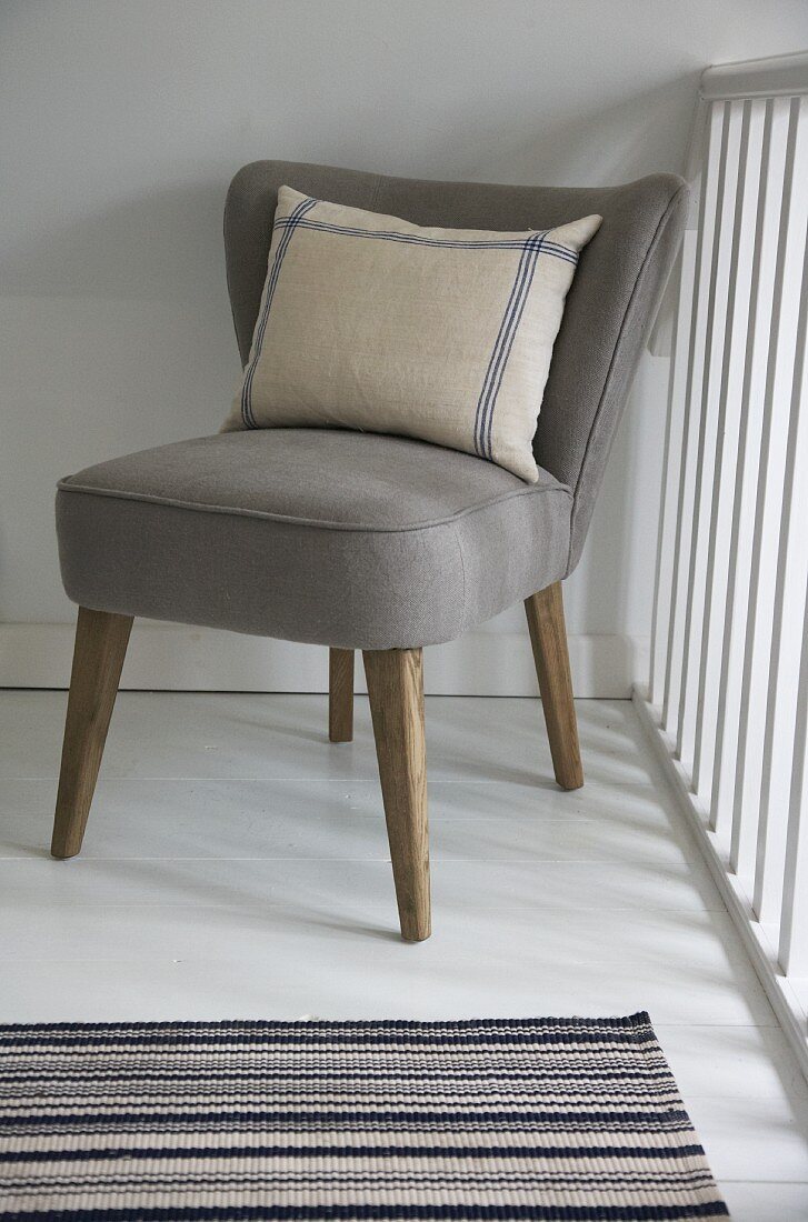 Striped linen cushion on retro easy chair with taupe upholstery; striped, woven rug in foreground
