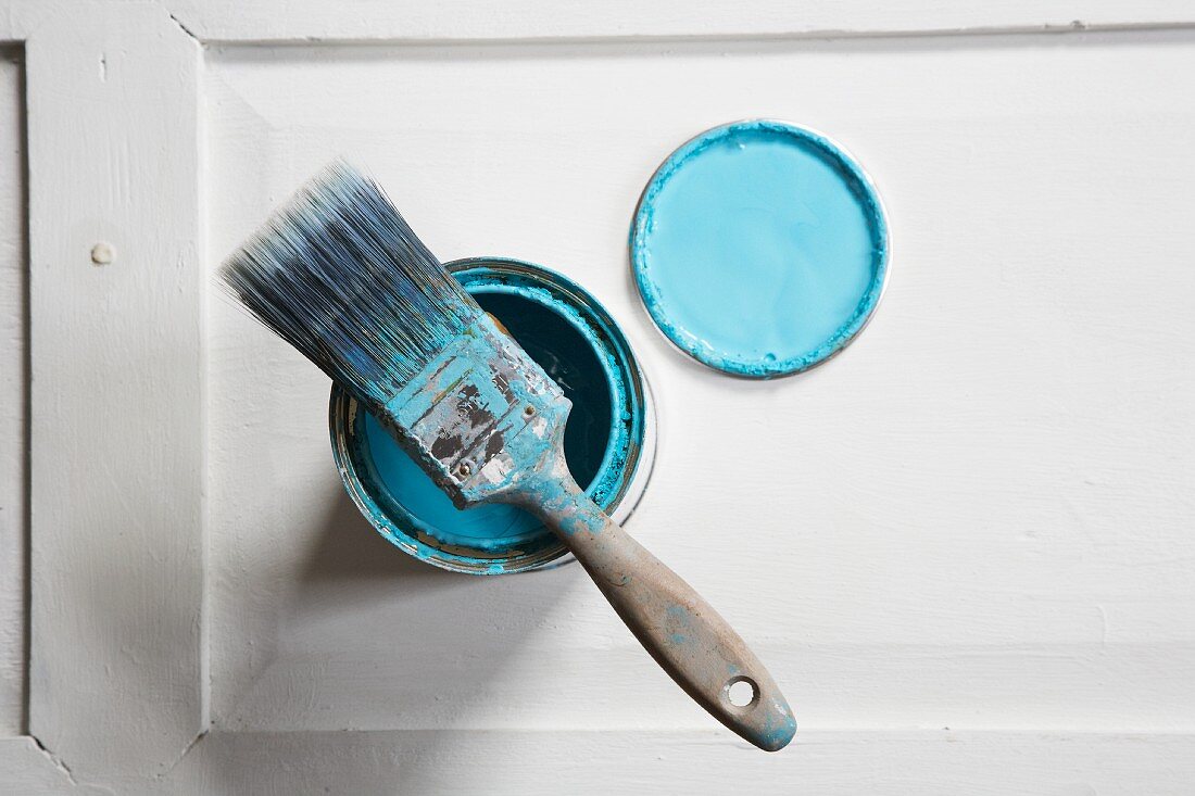 Flat paintbrush with pastel blue paint residue on open pot of paint