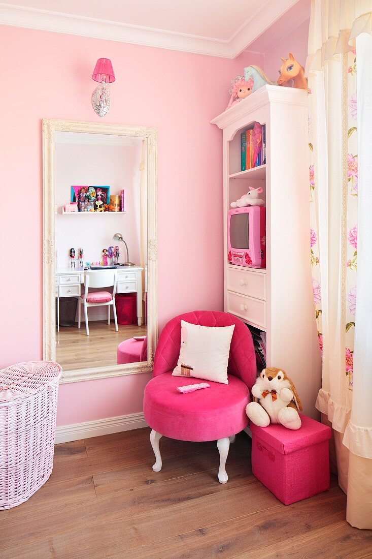weiße Möbel im Antikstil und Sessel in kräftigem Pink vor der zartrosa getönten Wand eines Mädchenzimmers