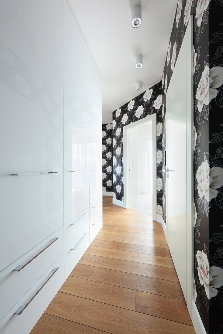 A crocked hallway with shiny, built-in cupboards and black and white floral wallpaper