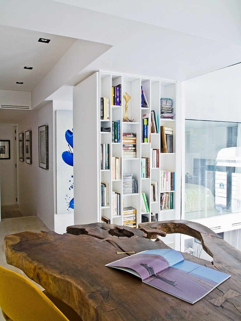 Rustikale, naturbelassene Holzplatte auf Tisch, in modernem Wohnzimmer, im Hintergrund weisses Regal