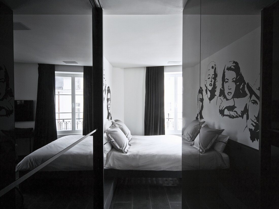 Blick durch schmalen Gang, Reflexionen auf spiegelnder Schrankoberfläche und Blick ins Schlafzimmer mit Doppelbett
