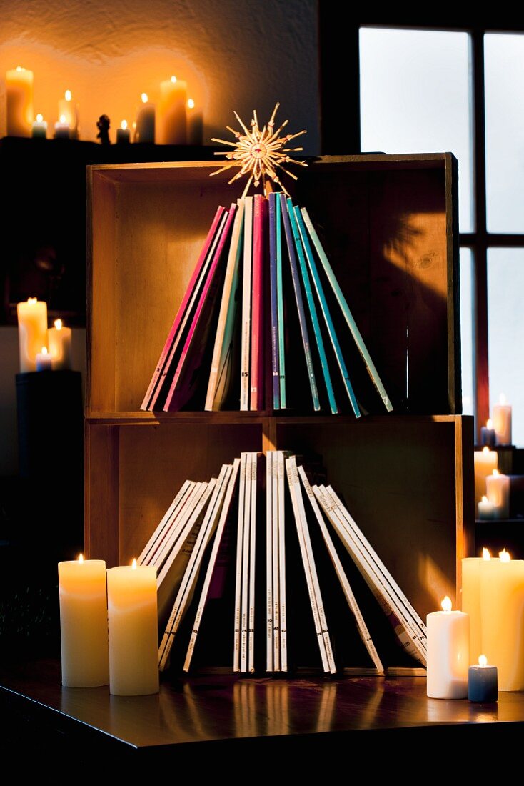 Arrangement in Weihnachtsbaumform mit Zeitschriften und Strohstern in alten Holzkisten, dazu viele brennende Kerzen