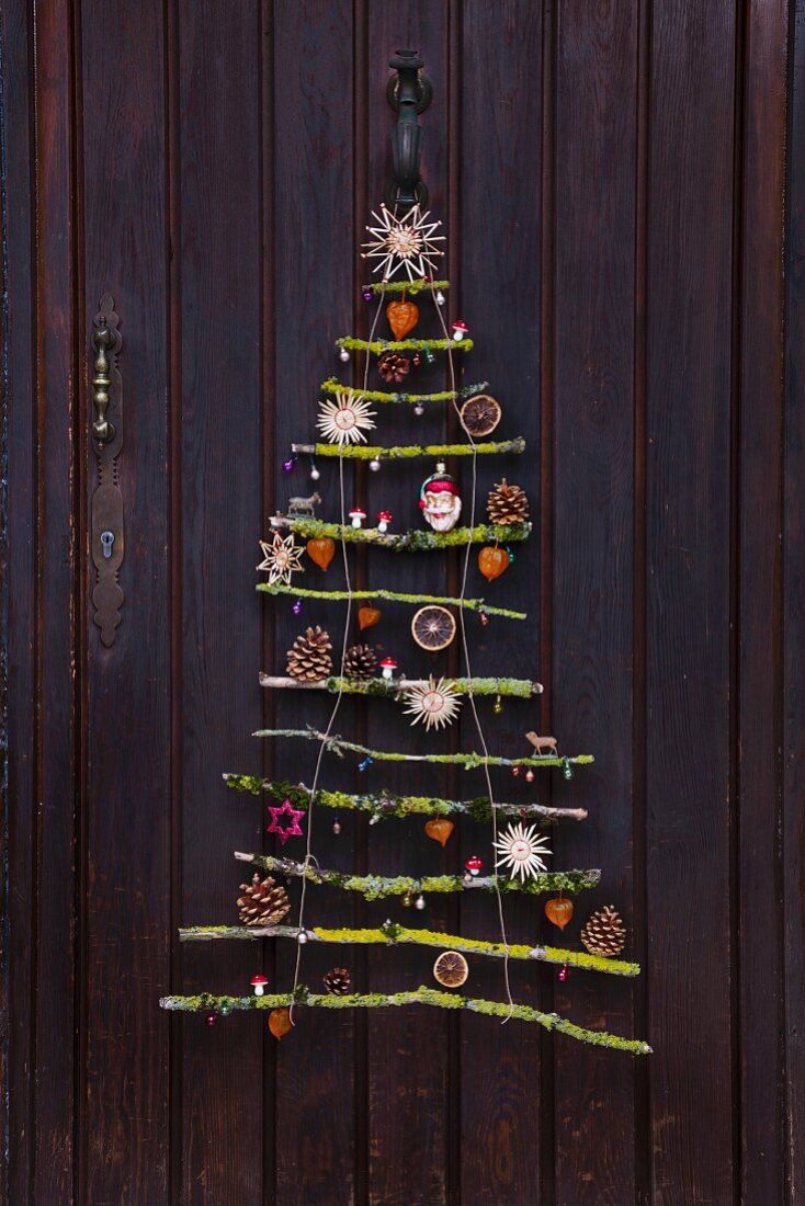 Stilisierter Weihnachtsbaum aus vermoosten Ästen mit Naturdeko und Strohsternen an einer Haustür