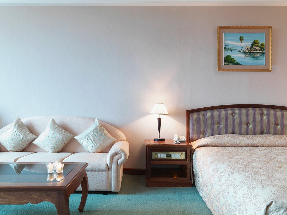 Doppelbett, Nachtkonsole & Sofa mit Dekokissen in Hotelzimmer