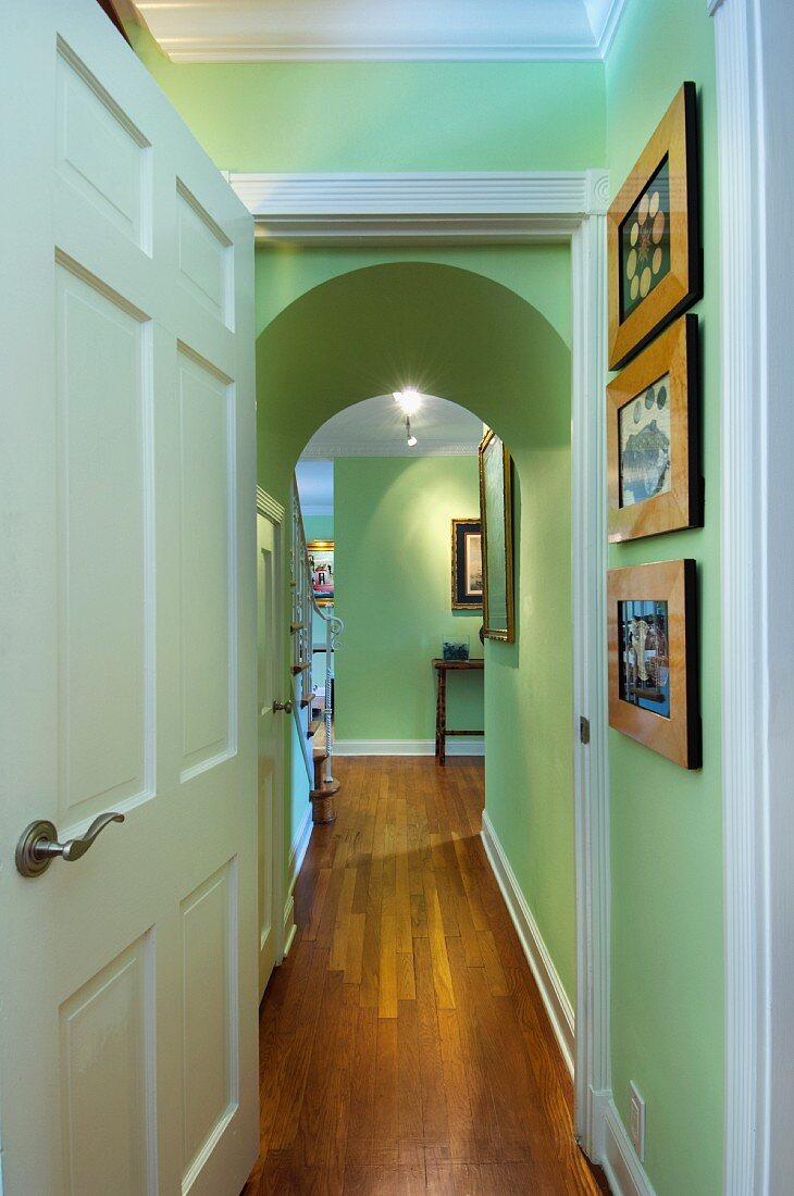 Blick durch geöffnete Tür in schmalen Flur mit grünen Wänden, Rundbogen & Holzboden