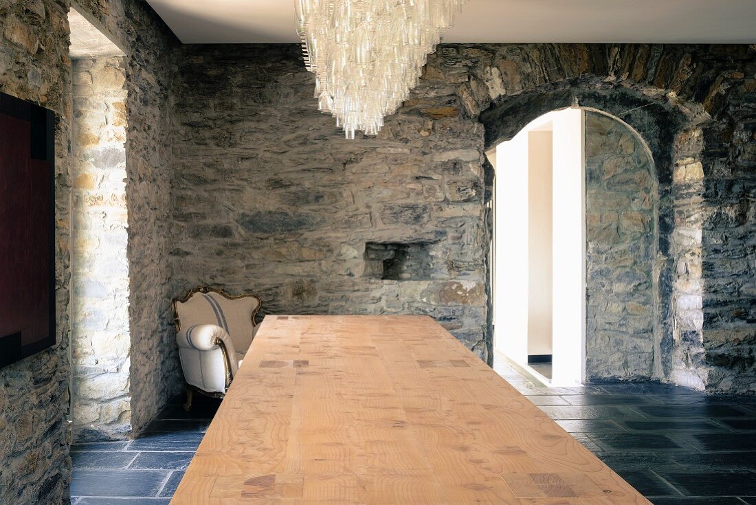 Lüster über ausladender Tischplatte und barocker Sessel vor den rustikalen Natursteinwänden eines ligurischen Rustico