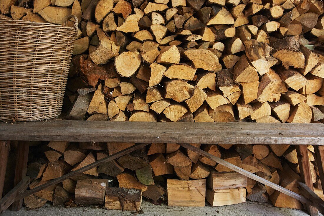 Rustikale Holzbank und Weidenkorb vor geschichtetem Holzlager