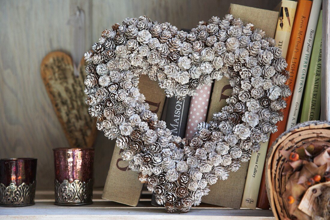 Heart-shaped wreath of silver-painted larch cones in front of books on shelf
