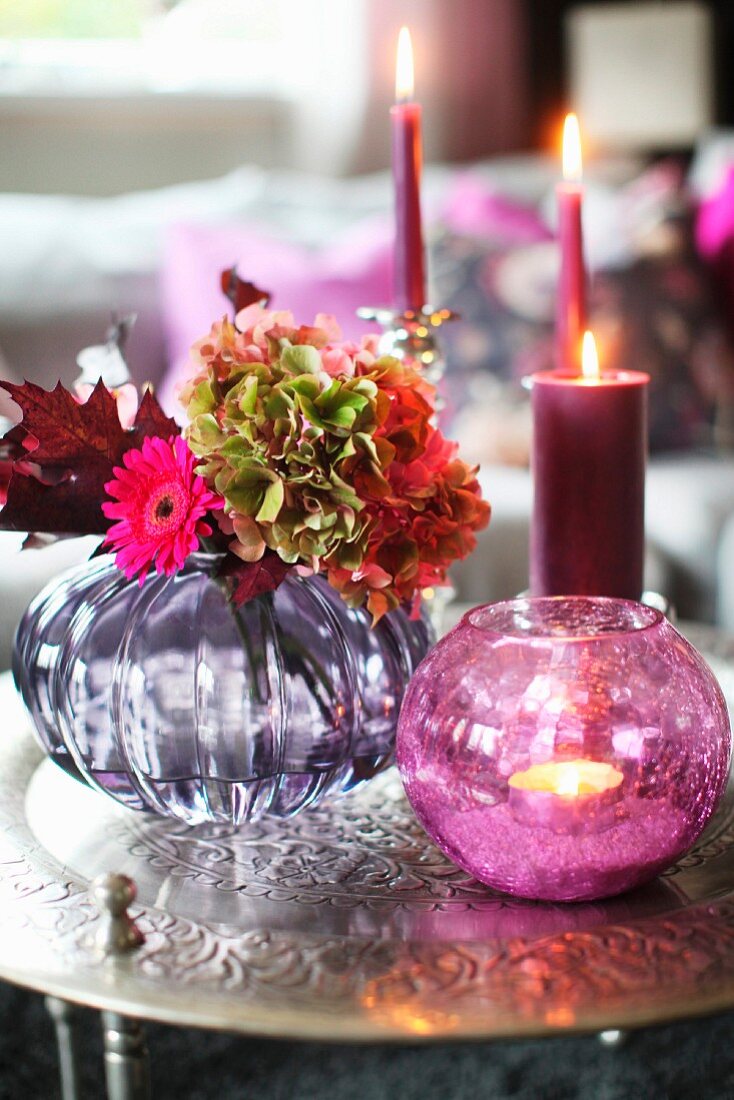 Romantic, autumnal flower arrangement and lit candles on antique metal table