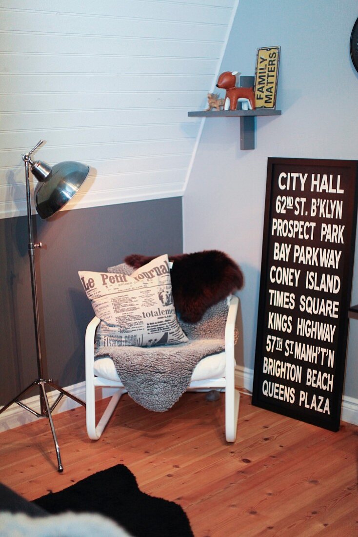 Teenager's bedroom in grey and white with wooden floor, comfortable reading chair with sheepskins and black and white picture with lettering leaning on wall